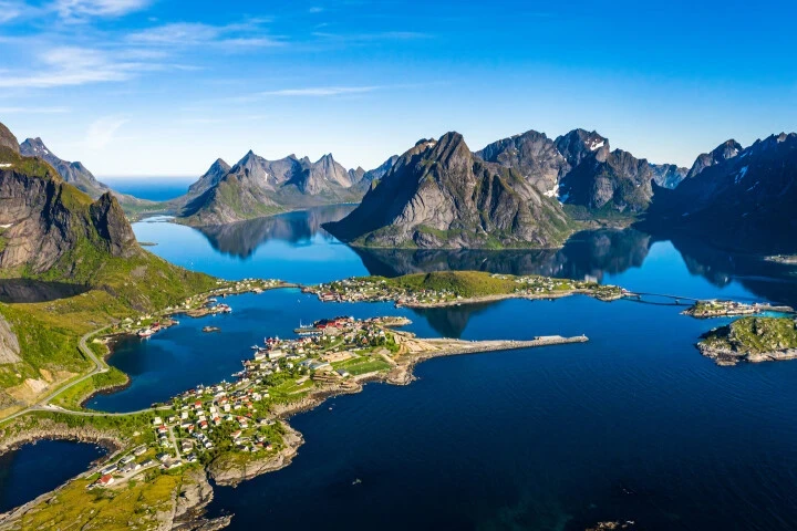 A stunning aerial view of a Norwegian fjord surrounded by dramatic mountains and charming coastal villages, highlighting the breathtaking landscapes of sailing holidays in Norway.